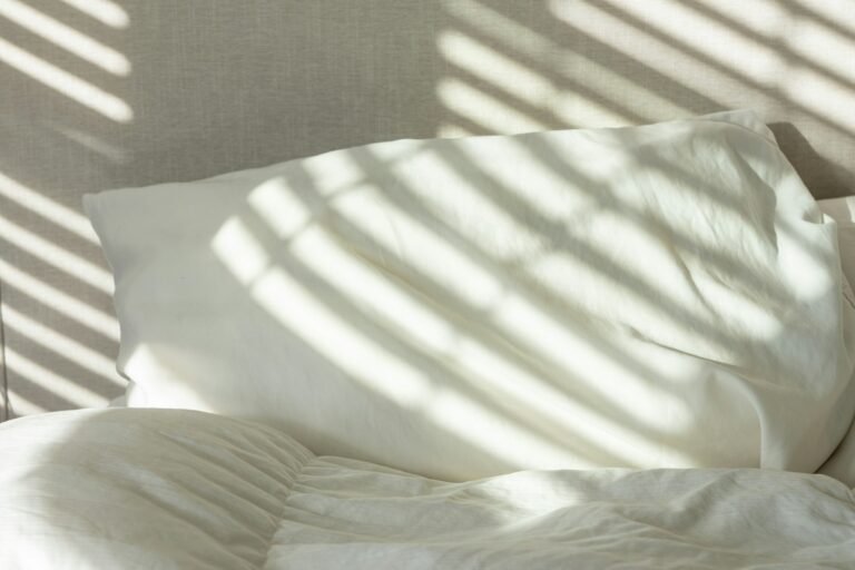 Freshly made bed with crisp white sheets in morning sunlight after a deep cleaning